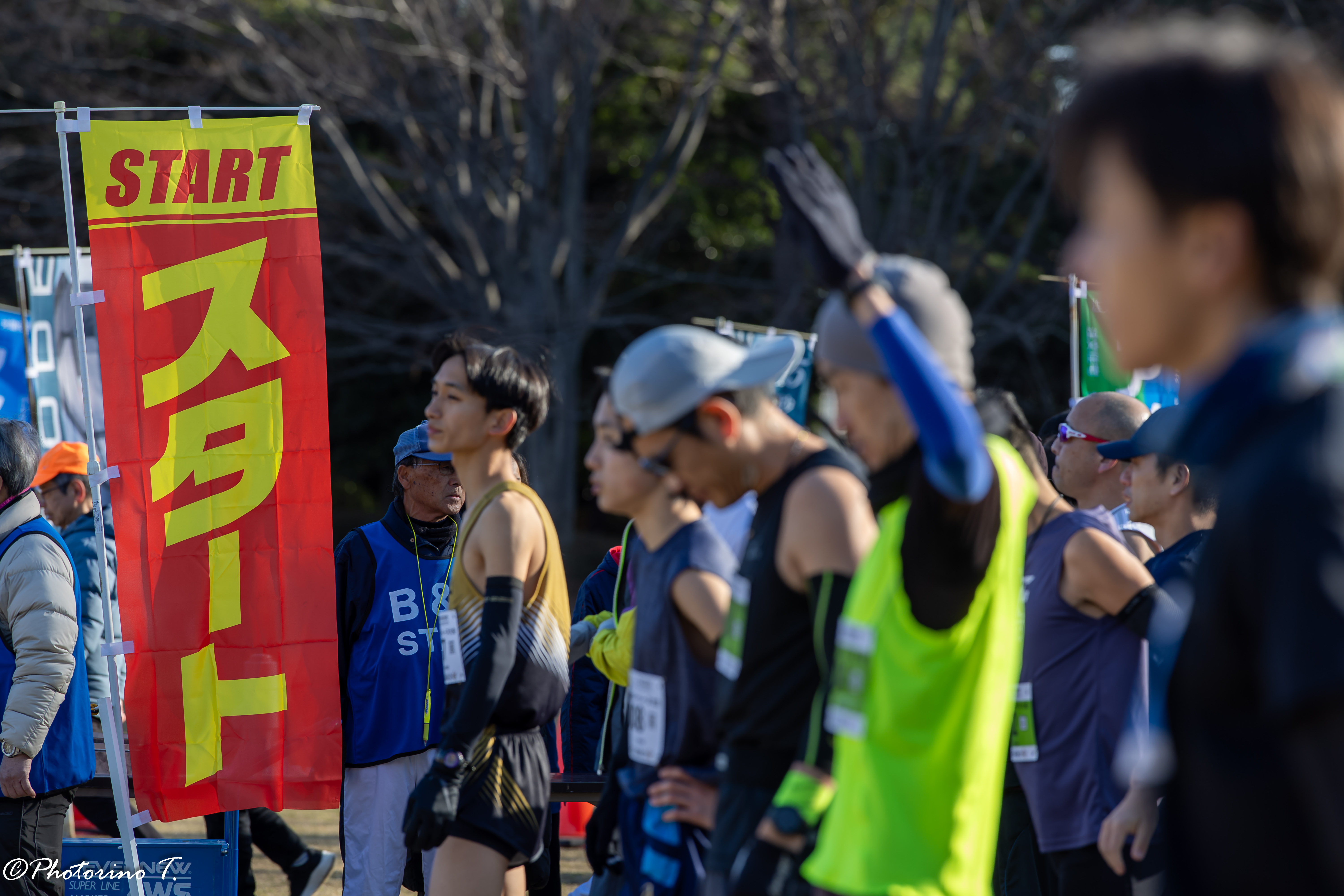 マラソンのスタート地点でゼッケンを付けた複数のランナーと赤いSTARTの旗が並ぶ
