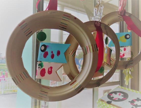 窓辺に飾られたカラフルな魚のデザインが施された紙製のリースが三つ並んでいる画像。
