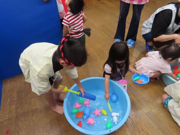 こどもたちが水の中でカラフルなおもちゃをつかまえようとしている様子。