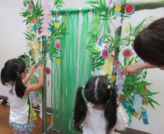こどもたちが装飾された竹の前で短冊を飾り付けている様子。