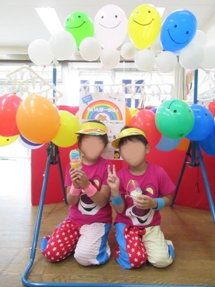 カラフルな風船の前でアイスクリームを持つ二人のこどもがポーズをとっている写真。