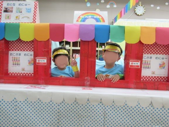 こどもたちがカラフルな屋台の窓から顔を出している写真。