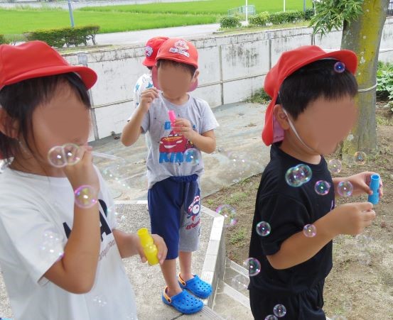 赤い帽子をかぶった子どもたちが泡を吹いて遊んでいる様子。