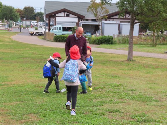 こどもたちが大人と一緒に公園の芝生で遊んでいる様子
