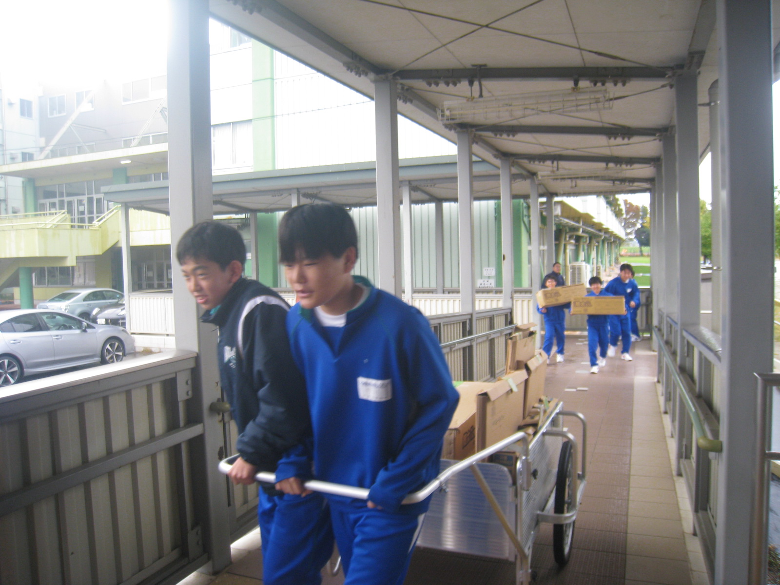 青い作業服を着た数人の人々が廊下を歩き、荷物を運んでいる様子を示す画像です