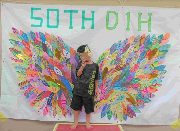 羽の形の記念作品の前でポーズを取るこども