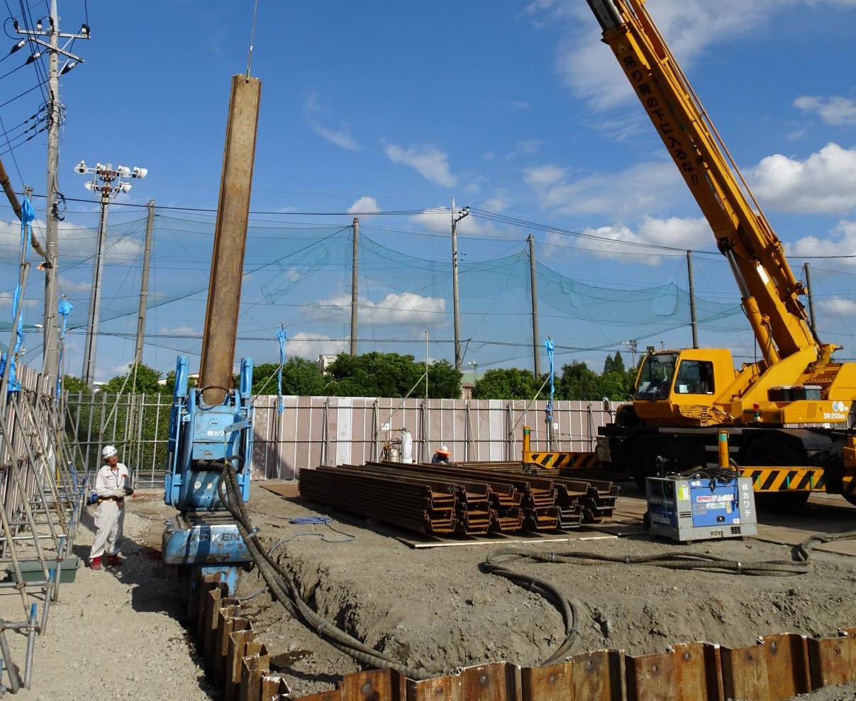 建設現場で黄色いクレーンと青い作業用リフトが並び作業員がコンクリートの基礎で作業している様子