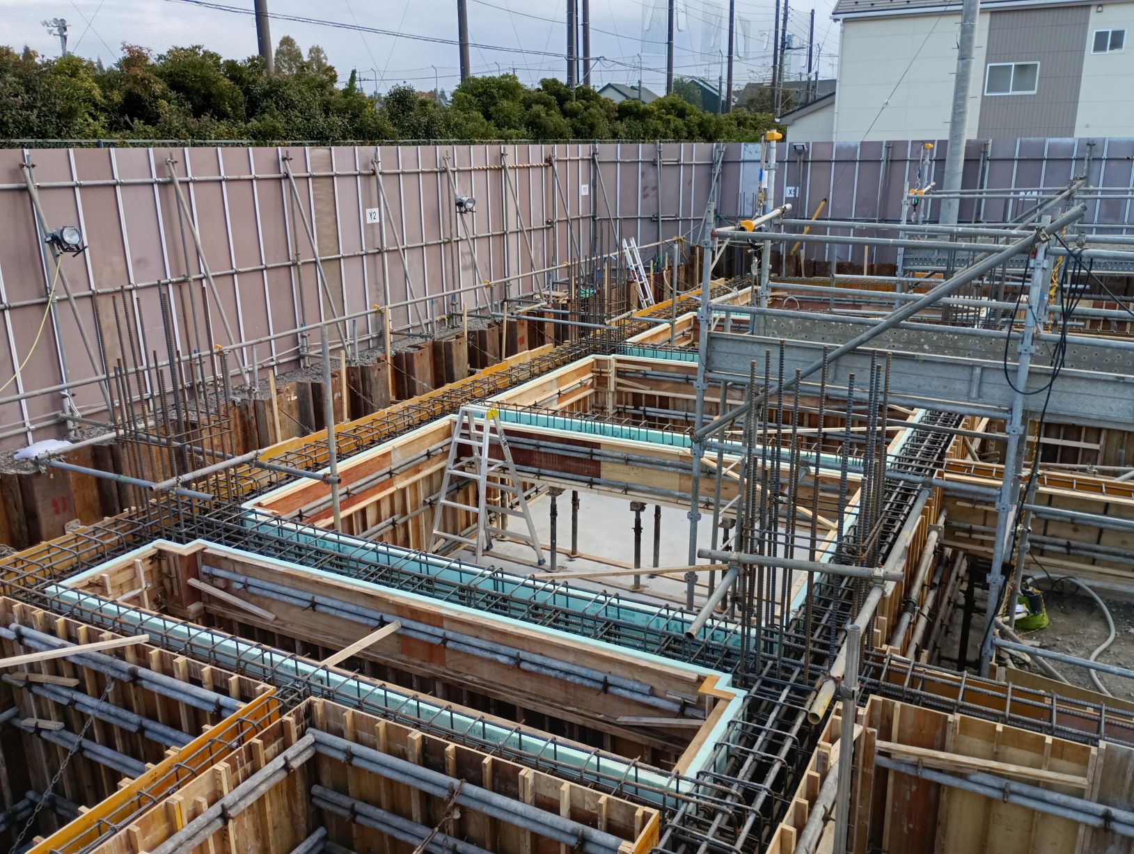 建設現場の基礎工事で鉄筋と型枠と足場が複雑に組まれ中央付近に脚立が置かれている