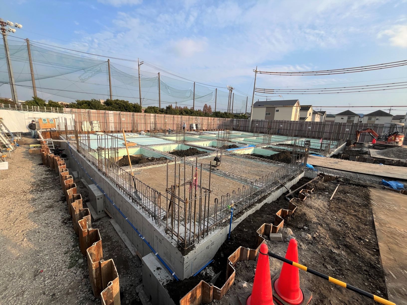 住宅地の中でコンクリート基礎の配筋と工事用コーンが置かれた建設現場の風景