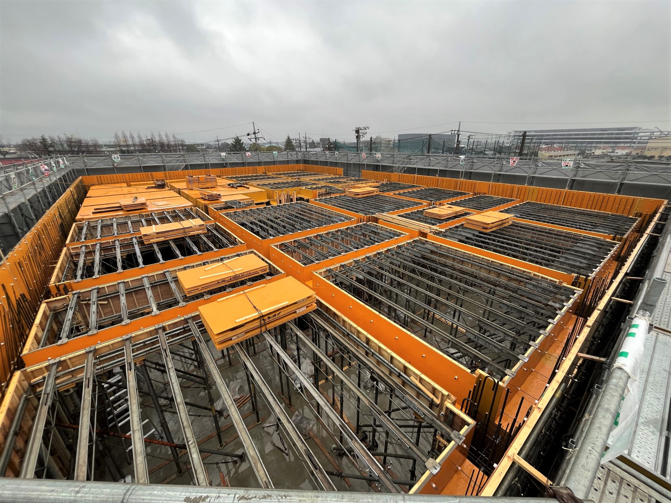 オレンジ色の型枠と鉄筋が格子状に並ぶ建設中の建物の躯体