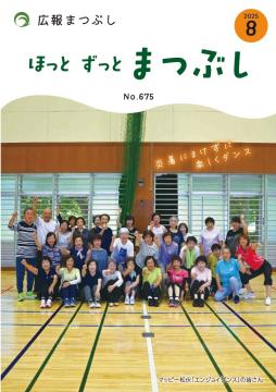 体育館の床に並んで座り立つ多世代の人々のグループ写真で背景に窓とカーテンがある