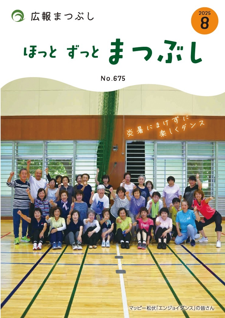 体育館の床に並んで座り立つ多世代の人々のグループ写真で背景に窓とカーテンがある