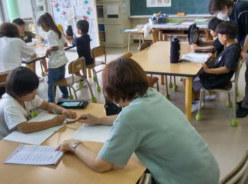 教室で机に向かい学習する子どもたちに寄り添いノートを指導する指導員と複数の生徒がいる風景