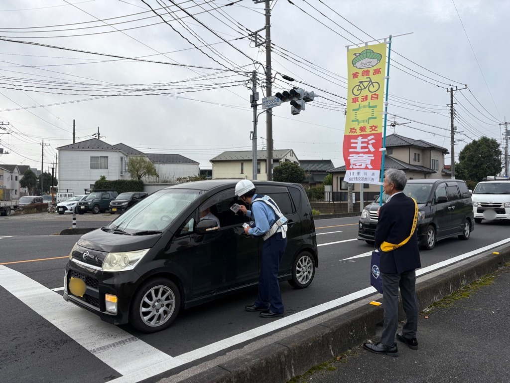 交差点で小型車の窓越しに立つ制服の警察官がドライバーに声をかけている風景